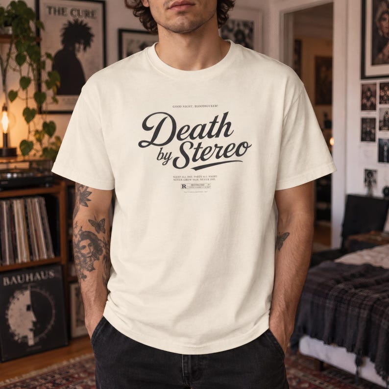 A person with tattooed arms wears an off-white t-shirt with black Death by Stereo text against a bright background.