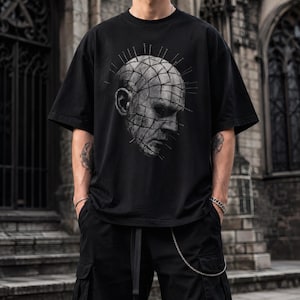 May include: A black short-sleeved t-shirt featuring a large, detailed graphic print on the chest. The design depicts a monochromatic, grid-patterned human head with numerous thin, sharp spikes protruding from the surface, creating a textured effect.