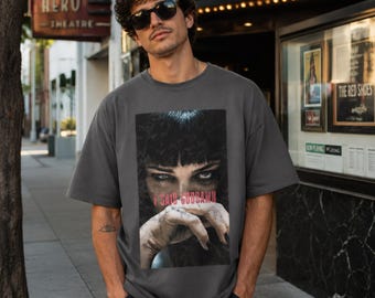May include: A charcoal gray short-sleeve t-shirt featuring a large rectangular graphic print on the chest. The print displays a close-up of a person with dark hair and intense eyes, with the red text I SAID GODDAMN printed across the center.