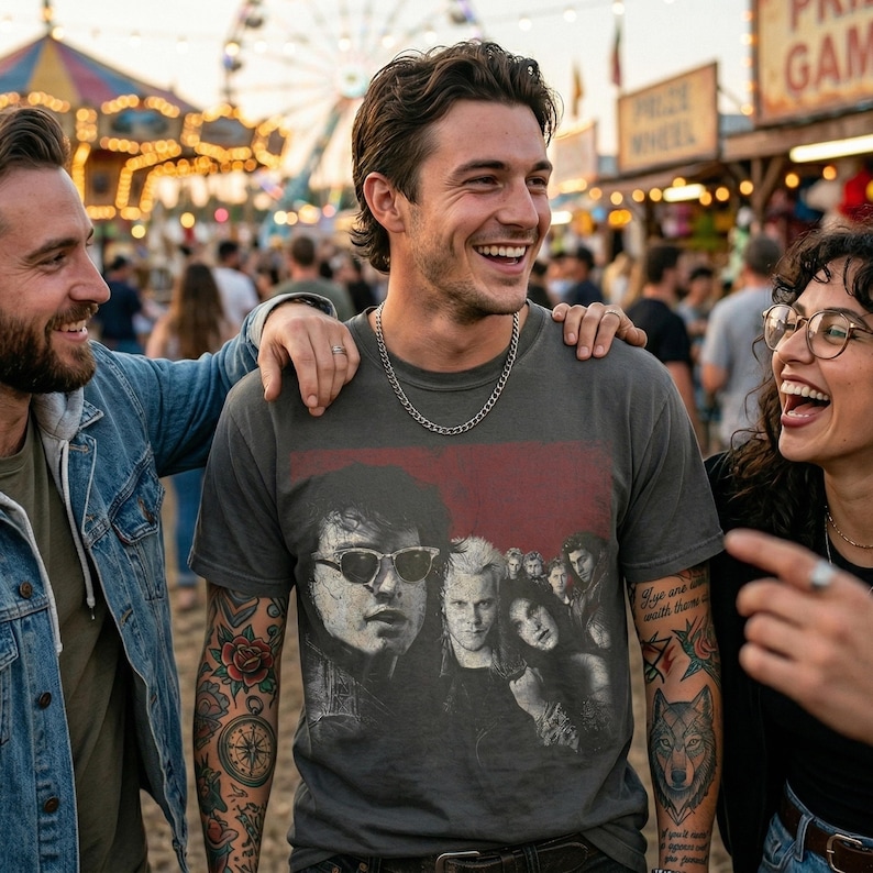 A man wearing a dark gray t-shirt with a graphic of five people in a red box, smiling with two other people at a carnival.