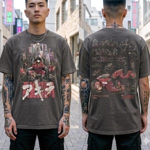 May include: Dark grey t-shirt with a graphic from the anime Akira. The front features a red character and Japanese text. The back shows motorcycle illustrations and the text "CAPSULE GANG 1986".