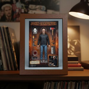 May include: A framed John Carpenter action figure set. The figure wears a black jacket and blue jeans. Accessories include a miniature keyboard, axe, and a Michael Myers mask. The packaging includes the text "Everyone's entitled to one good scare."