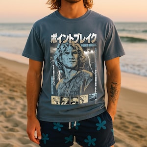 Puede incluir: Una camiseta azul grisáceo con un gráfico de la película "Point Break" y texto japonés. El gráfico incluye un retrato de un hombre con pelo largo y rayos. La persona de la imagen lleva pantalones cortos azul marino con un estampado floral.
