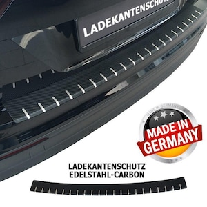 Può includere: Un paraurti di un'auto nero con un aspetto in fibra di carbonio e una finitura argentata. Il paraurti ha il testo "Ladekantenschutz Edelstahl-Carbon" e un adesivo che dice "Made in Germany".