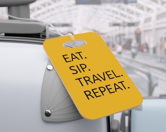 Op de afbeelding: Geel bagagelabel met de tekst "EAT. SIP. TRAVEL. REPEAT." op een witte koffer.