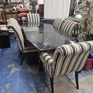 May include: A black marble dining table with six chairs. The chairs feature black and beige striped upholstery and black legs. The table is rectangular with a marble effect. The chairs are positioned around the table.