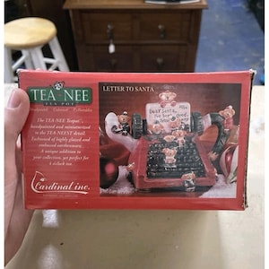 May include: A rectangular red product box for a Tea-Nee Teapot titled Letter to Santa. The box features a graphic of a ceramic teapot shaped like a vintage typewriter with small teddy bears, and text including Cardinal Inc. and Tea-Nee Teapot.