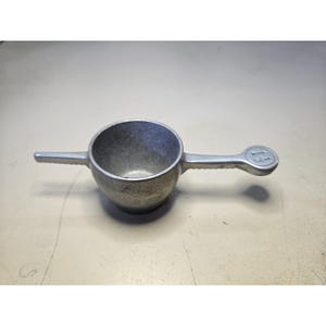 May include: A silver-colored metal measuring cup with a round bowl, a pointed spout on one side, and a flat handle on the opposite side. The handle features a circular end with the embossed fraction 1/2 clearly visible on its top surface.