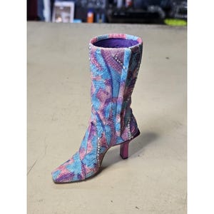 May include: A mid-calf boot featuring a multi-colored snakeskin-like pattern in shades of blue, purple, and pink. The boot is embellished with rows of clear rhinestones along the seams and has a square toe with a slim, dark pink kitten heel.
