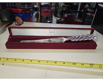 May include: A silver-toned metal letter opener with a clear, faceted crystal handle, presented in a long, rectangular, burgundy velvet-lined box with the Mikasa logo printed inside. A yellow measuring tape shows the item is 12 inches long.