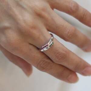 May include: A silver ring with a row of small pink and green gemstones.