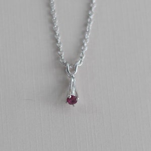 May include: A delicate silver chain necklace with a small, red gemstone pendant.