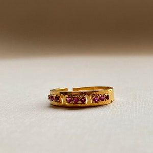 May include: A gold ring with a band of small pink gemstones.