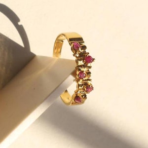 May include: A gold ring with a row of small pink gemstones. The ring is on a white surface.
