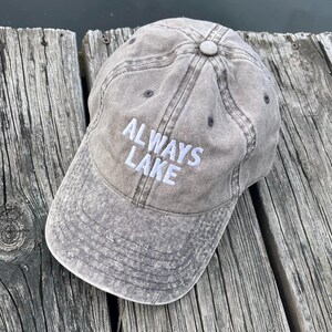 May include: A brown, distressed, cotton baseball cap with white embroidery that reads "ALWAYS LAKE".