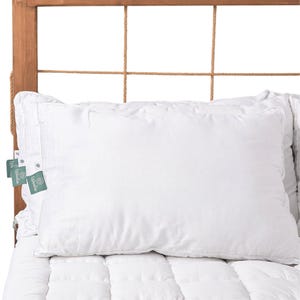 May include: A white pillow with a white button and a green label that says "La Woodie" on a white bed with a wooden headboard.