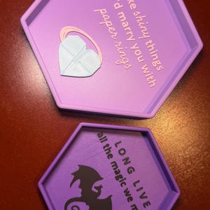 May include: Two hexagonal purple trays. The top tray has the text "I like shiny things but I'd marry you with paper rings" and a heart-shaped accessory. The bottom tray has a dragon silhouette and the text "LONG LIVE all the magic we made."