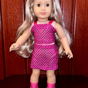 May include: A doll wearing a pink sequined dress and pink boots. The doll has long blonde hair and brown eyes.