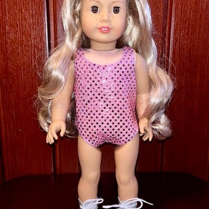 May include: A pink sequined leotard with a scoop neck and a fitted silhouette. The leotard is worn by a doll with blonde hair and silver boots.