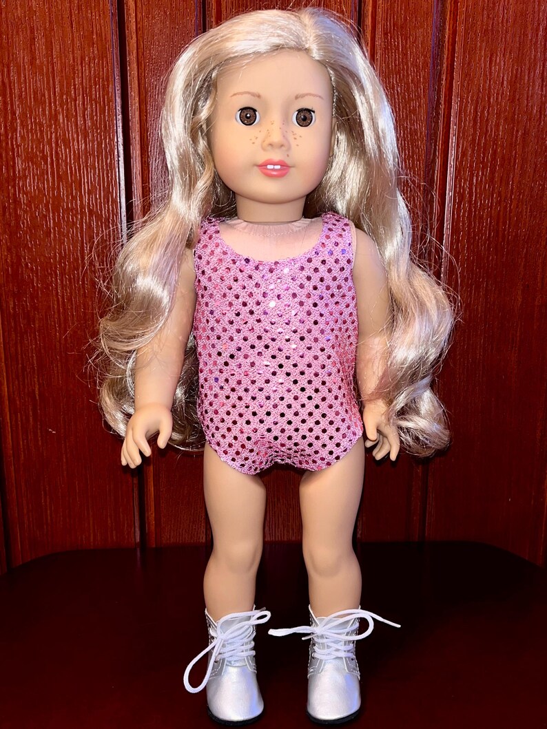 May include: A pink sequined leotard with a scoop neck and a fitted silhouette. The leotard is worn by a doll with blonde hair and silver boots.