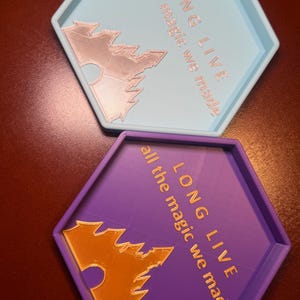 May include: Two hexagonal trays, one light blue and one purple, with raised edges. Each tray features the text "LONG LIVE all the magic we made" and a stylized bat design. The text and bat are in a contrasting color.