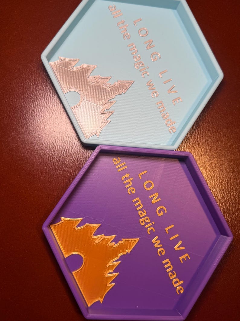 May include: Two hexagonal trays, one light blue and one purple, with raised edges. Each tray features the text "LONG LIVE all the magic we made" and a stylized bat design. The text and bat are in a contrasting color.