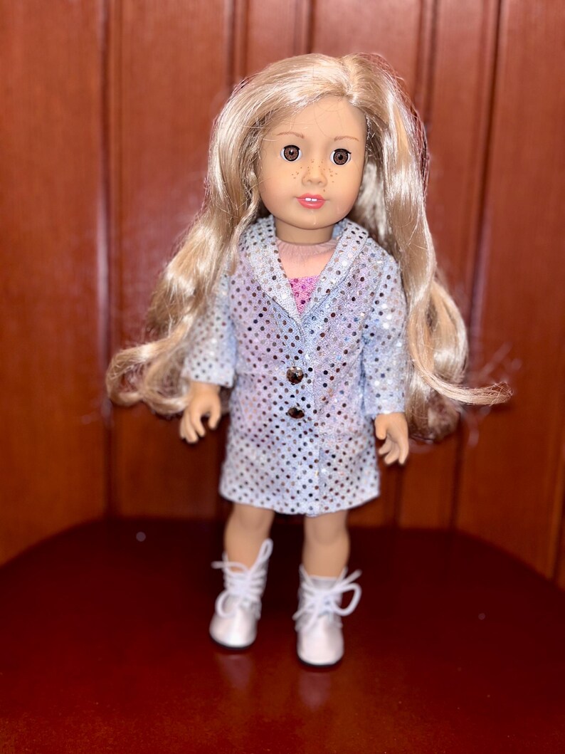 May include: A doll with long blonde hair wearing a silver sequined dress and white boots.