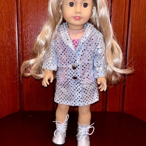 May include: A silver sequined jacket and dress outfit for a doll. The doll has blonde hair and brown eyes. The outfit has a button closure and a collar.