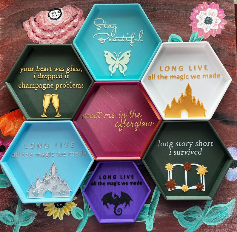 May include: A collection of seven hexagonal trays in various colors, each with a unique design and text. The trays feature phrases like "Stay Beautiful" and "Long Live," along with decorative elements such as a butterfly and a castle.