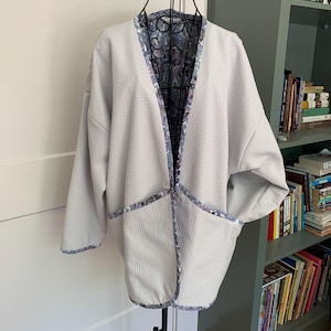 May include: A light gray waffle-weave jacket with a floral print lining. The jacket has a V-neck and long sleeves.