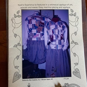 May include: A package for a quilted winter dress pattern titled "Follow the Leader." The pattern features a whimsical applique of an ark, animals, and waves. The dress has a blue and white checkered skirt.