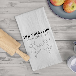 May include: White kitchen towel with the text "HOLY ROLLERS Saints of the Dough" and a design of six rolling pins with angel wings.