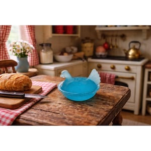 May include: A blue glass chicken-shaped bowl sits on a wooden table. The bowl is filled with a blue liquid. A loaf of bread and a knife rest on a wooden cutting board. The scene is set in a miniature kitchen with a red and white checkered tablecloth.
