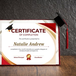 Puede incluir: Un certificado de finalización rojo y dorado con un icono de gorro de graduación negro. El certificado se entrega a Natalie Andrew por completar una pasantía de cuatro meses como diseñadora gráfica en SrimberioFradel and Spies Co.