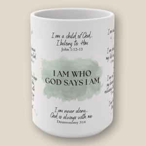 May include: A white ceramic mug featuring black printed text and a sage green watercolor-style background element. The text reads I AM WHO GOD SAYS I AM, along with various religious phrases and scripture references including John 1:12-13.