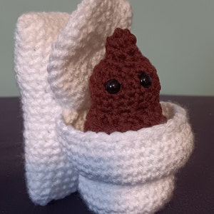 May include: A crocheted white toilet with a brown crocheted poop sitting inside. The toilet has a lid that is open.