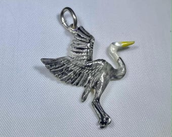 May include: A silver-toned metal pendant shaped like a bird in flight with outstretched wings. The bird features a white neck and a yellow beak, with detailed engraved feather textures across the body and wings, topped with a circular jump ring.