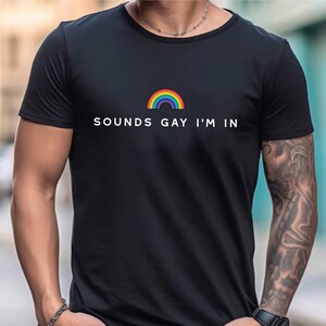 K&ouml;nnte beinhalten: Ein schwarzes T-Shirt mit einem Regenbogen-Motiv und dem Text "SOUNDS GAY I'M IN".