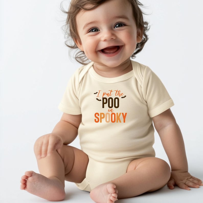 K&ouml;nnte beinhalten: Ein cremefarbener Kurzarm-Babybody mit dem Text I put the POO in SPOOKY in Braun und Orange, verziert mit kleinen schwarzen Fledermaus-Illustrationen. Das Kleidungsst&uuml;ck hat einen Rundhalsausschnitt und Druckkn&ouml;pfe im Schrittbereich.