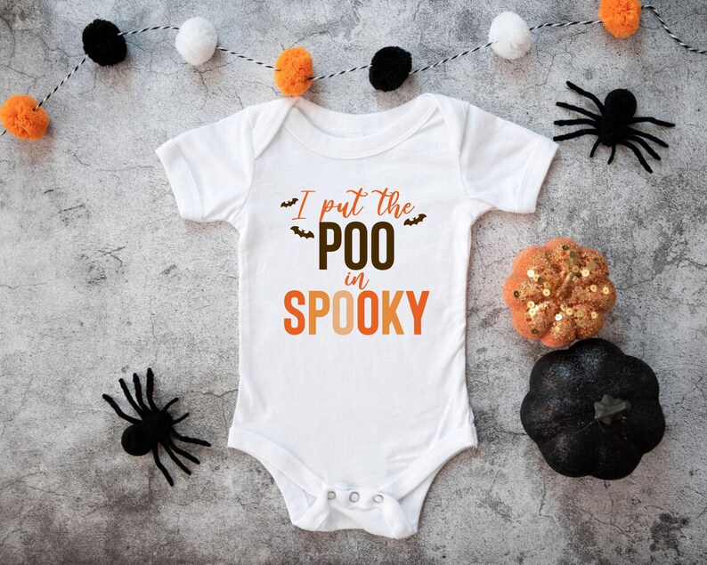 K&ouml;nnte beinhalten: Ein wei&szlig;er kurz&auml;rmeliger Babybody mit dem Schriftzug "I put the POO in SPOOKY" in braunen und orangefarbenen Buchstaben, verziert mit kleinen schwarzen Fledermausgrafiken. Das Kleidungsst&uuml;ck hat einen Rundhalsausschnitt und drei Druckkn&ouml;pfe.