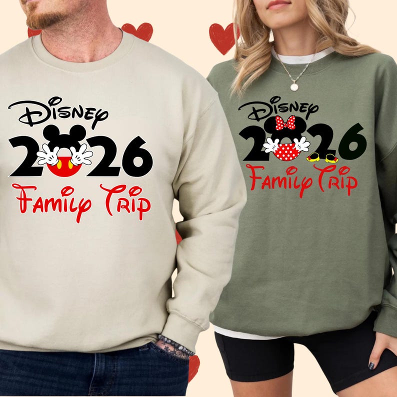 K&ouml;nnte beinhalten: Zwei lang&auml;rmlige Sweatshirts, eines beige und eines olivgr&uuml;n, mit einem Disney-Design. Das Design enth&auml;lt den Text "Disney 2026 Family Trip" mit Mickey Mouse-Bildern. Das beige Sweatshirt ist links, das gr&uuml;ne rechts.