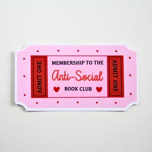 May include: A pink ticket-shaped sticker with the text "Membership to the Anti-Social Book Club." The sticker has a red border and red accents, including the words "Admit One" and two heart symbols. The background is white.