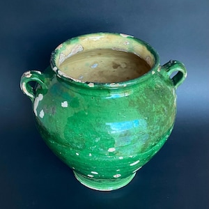 May include: A vintage, green ceramic pot with two handles. The pot has a wide opening and a rounded body. The exterior is a vibrant green with white and yellow accents, and the interior is a lighter shade of green.