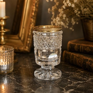 Peut inclure: Un récipient en verre transparent présentant un motif taillé en diamant sur la partie supérieure et une base lisse à facettes. Le bord supérieur est orné d'une bande métallique dorée texturée, contrastant avec le corps en verre.
