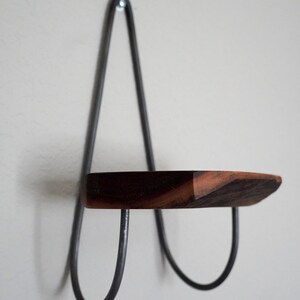 May include: A small wooden shelf with a metal frame. The shelf is attached to the wall with a single screw. The shelf is made of dark wood and the frame is made of black metal.