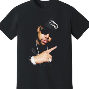 Peut inclure: T-shirt noir avec un imprimé graphique d'un homme portant un chapeau noir avec le mot "Foolish" écrit dessus, des lunettes de soleil et une chaîne en argent.