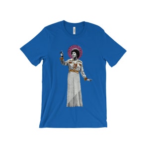 Könnte beinhalten: Ein königsblaues T-Shirt mit einem Aufdruck einer Frau in einem weißen und goldenen gemusterten Outfit. Die Frau steht mit erhobenem Arm und einem rosa und weißen Heiligenschein über ihrem Kopf.