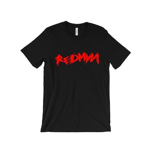 Puede incluir: Camiseta negra con la palabra "REDMAN" en rojo intenso y en negrita, con un diseño desgastado en el pecho. La camiseta es de manga corta y cuello redondo. El texto parece ligeramente texturizado.