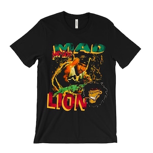 May include: Black t-shirt with a graphic design. The design features the words "MAD LION" in yellow, green, and red, along with an illustration of a person and a lion smoking a cigar.