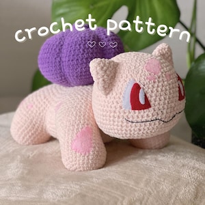 May include: Crochet pattern for a pink and purple Squirtle Pokemon amigurumi. The Squirtle is sitting on a white surface with the text "crochet pattern" above it.